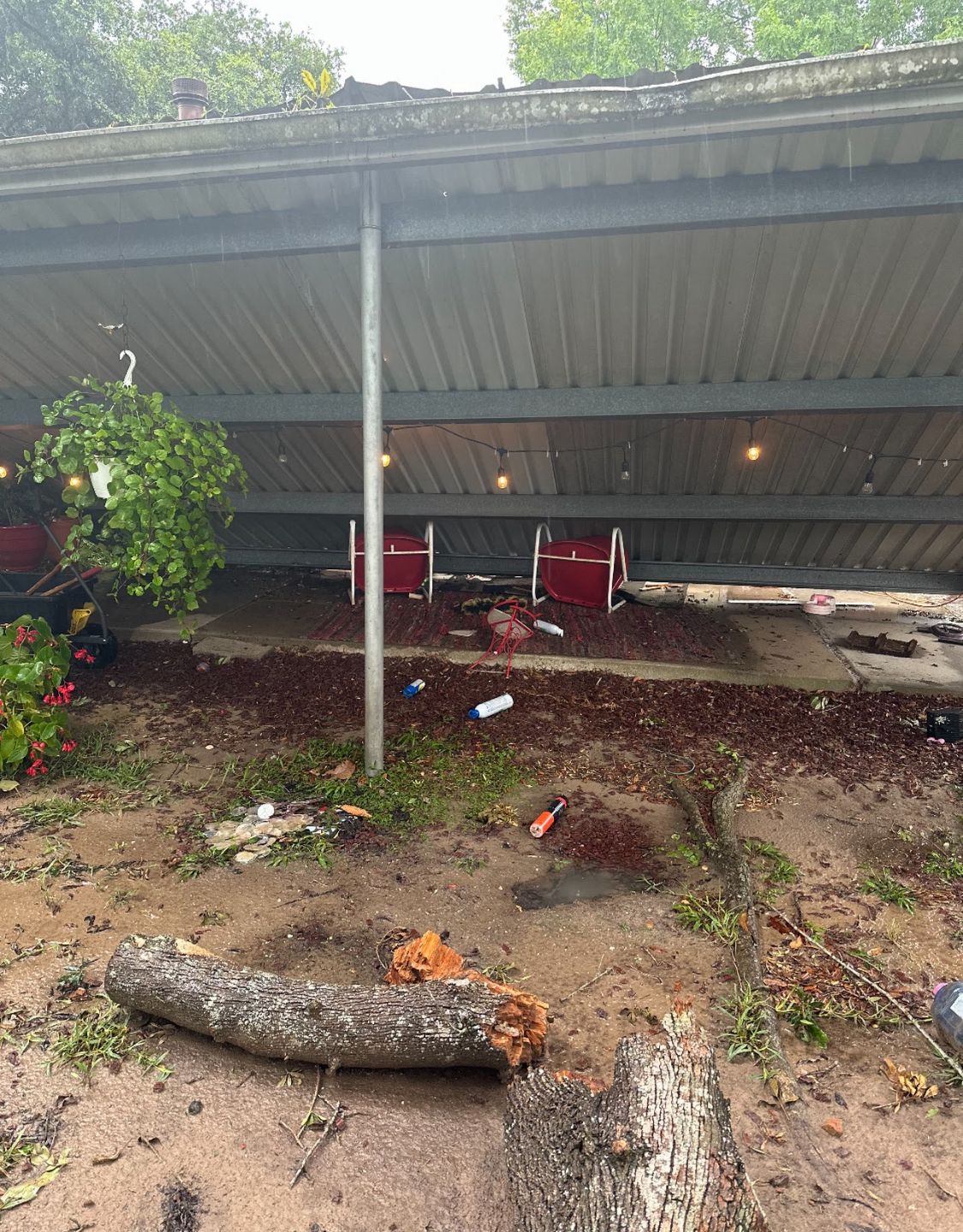 Collapsed carport roof over a yard with two red chairs and fallen debris underneath.