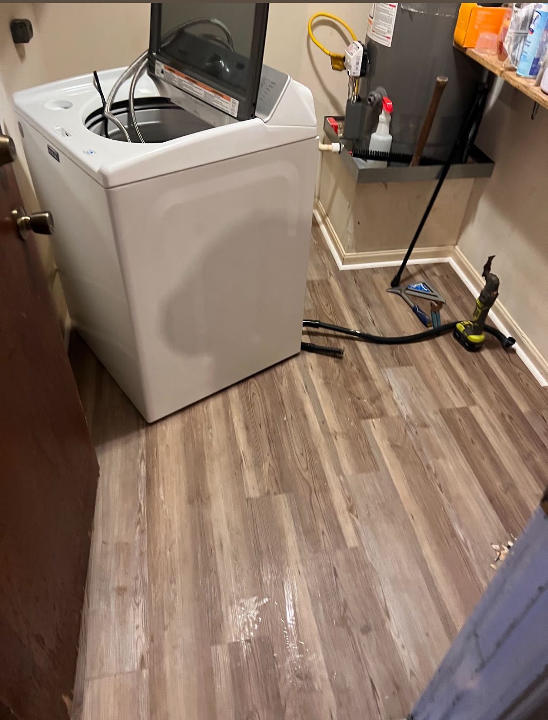 Laundry room with a white washing machine, exposed floor, and utility tools along the wall