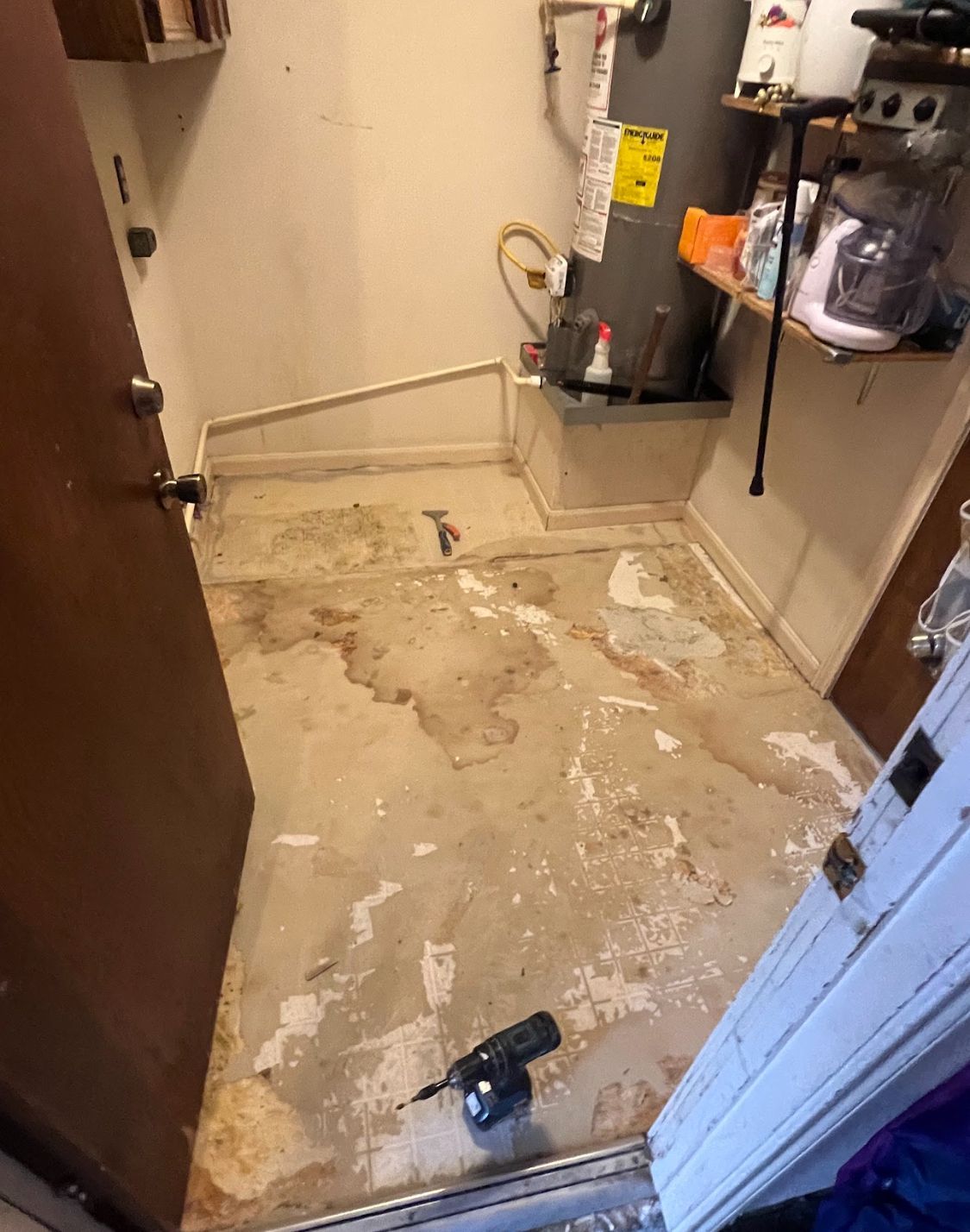 Damaged utility room floor with peeling tile, debris, and a drill near the doorway.