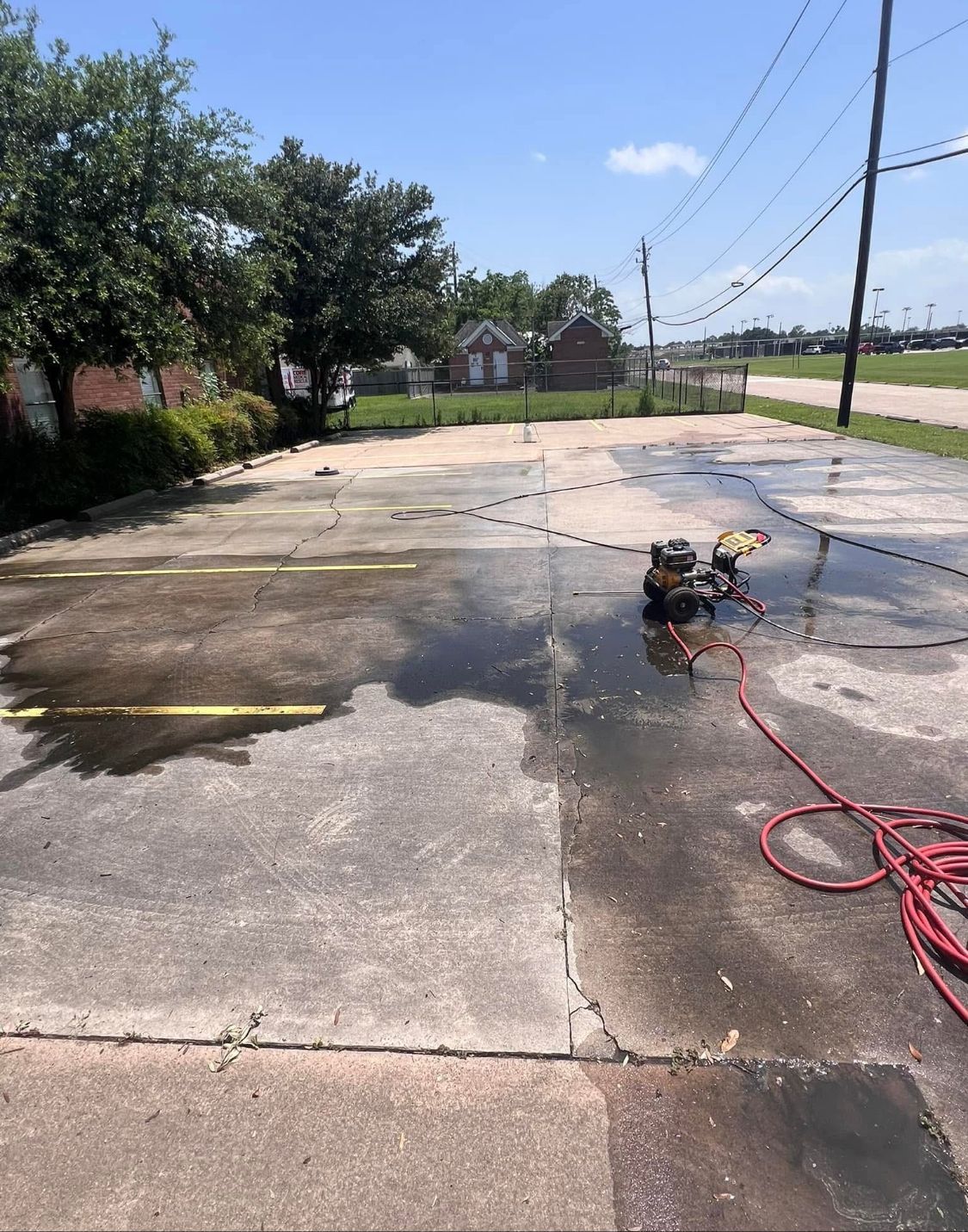 Driveway being pressure washed, with wet concrete, hose, and trees along a roadside.