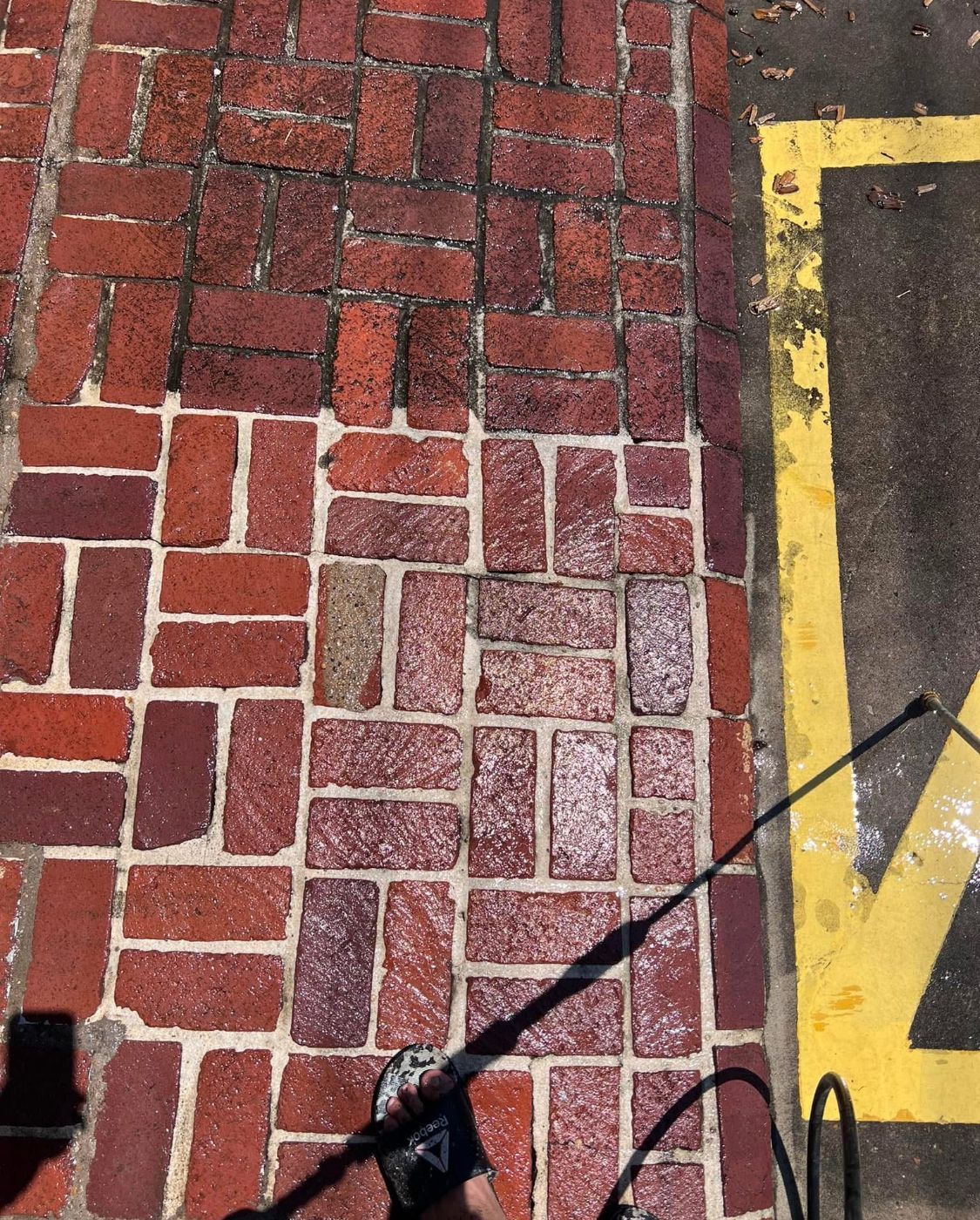 Brick sidewalk beside asphalt road with yellow line and a shadow crossing it