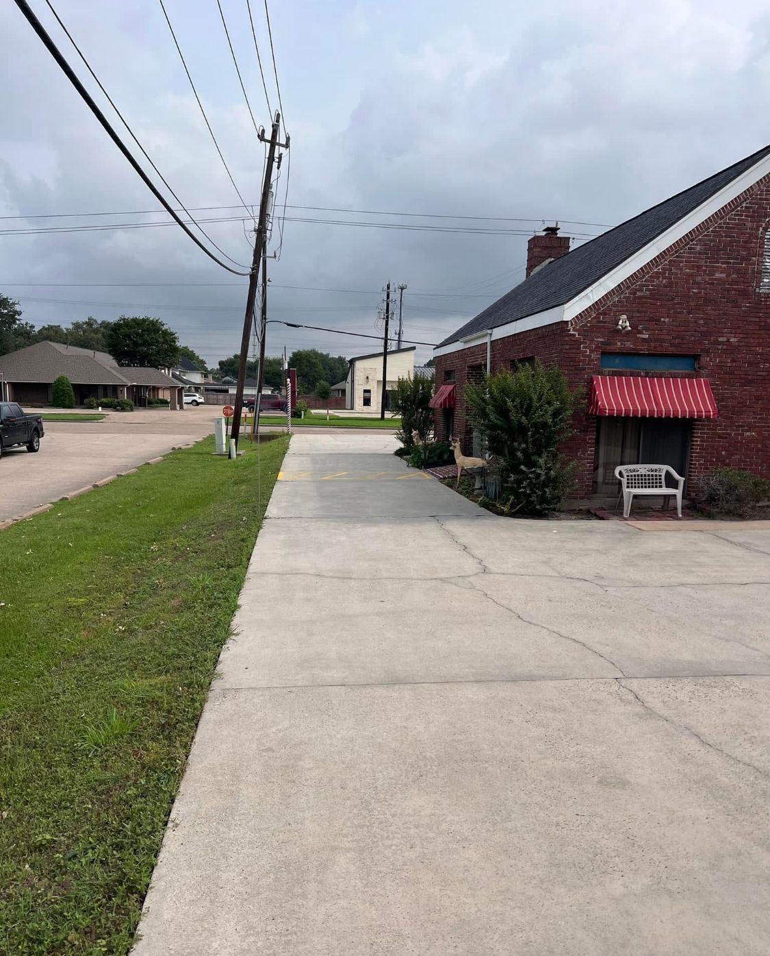 Sidewalk beside a red brick building with a red awning, grassy verge, utility poles, and cloudy sky.