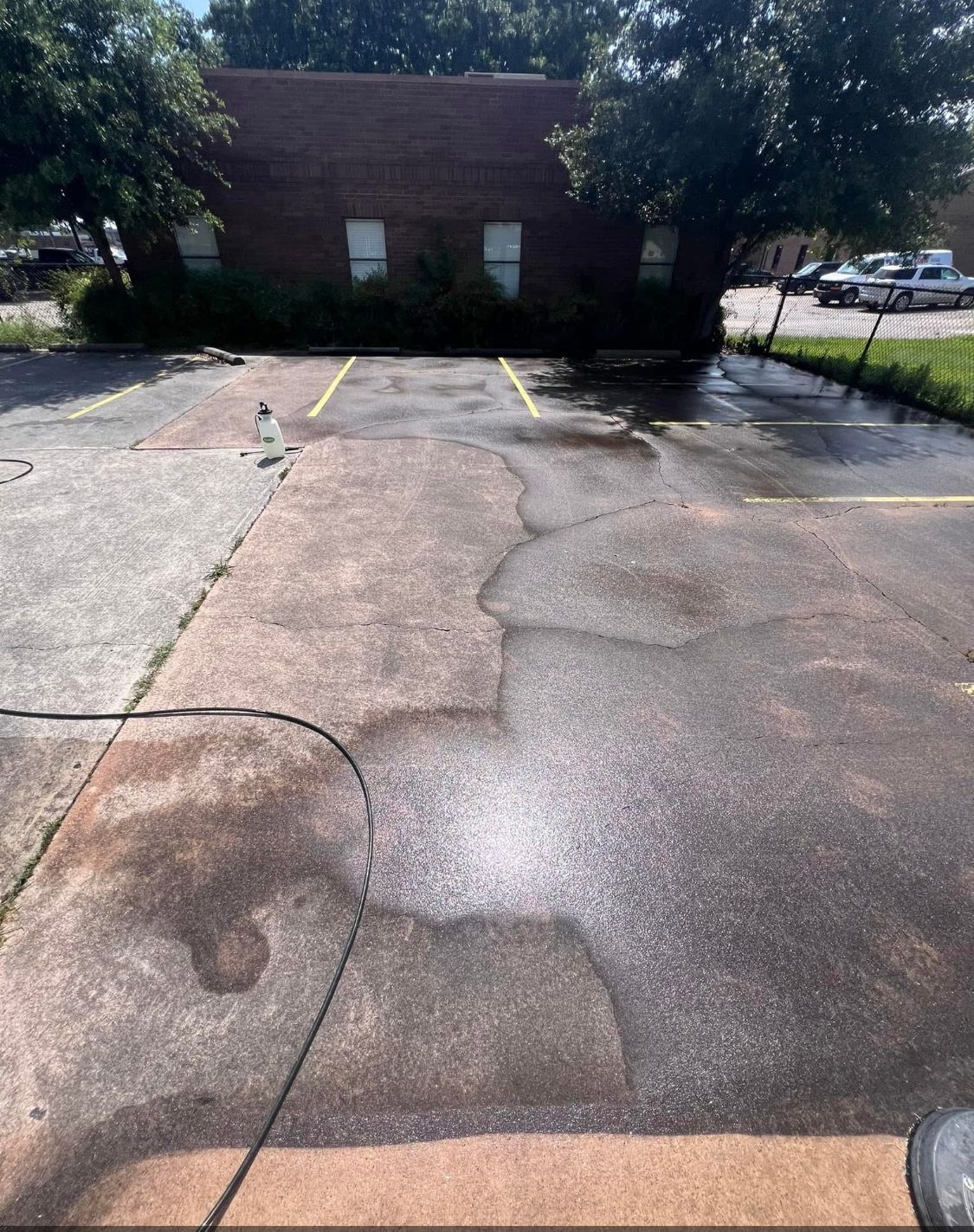 Cracked asphalt parking lot with puddles and a small brick building in the background