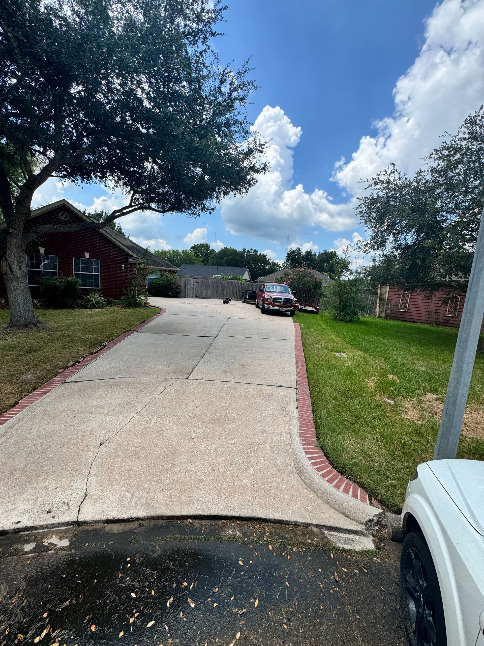 Steep concrete driveway beside red-brick house, with parked car at the top under a blue sky.