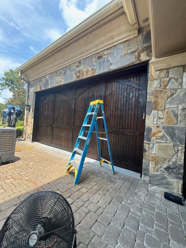 Blue ladder in front of a dark wooden garage door on a stone house, with a fan in the foreground