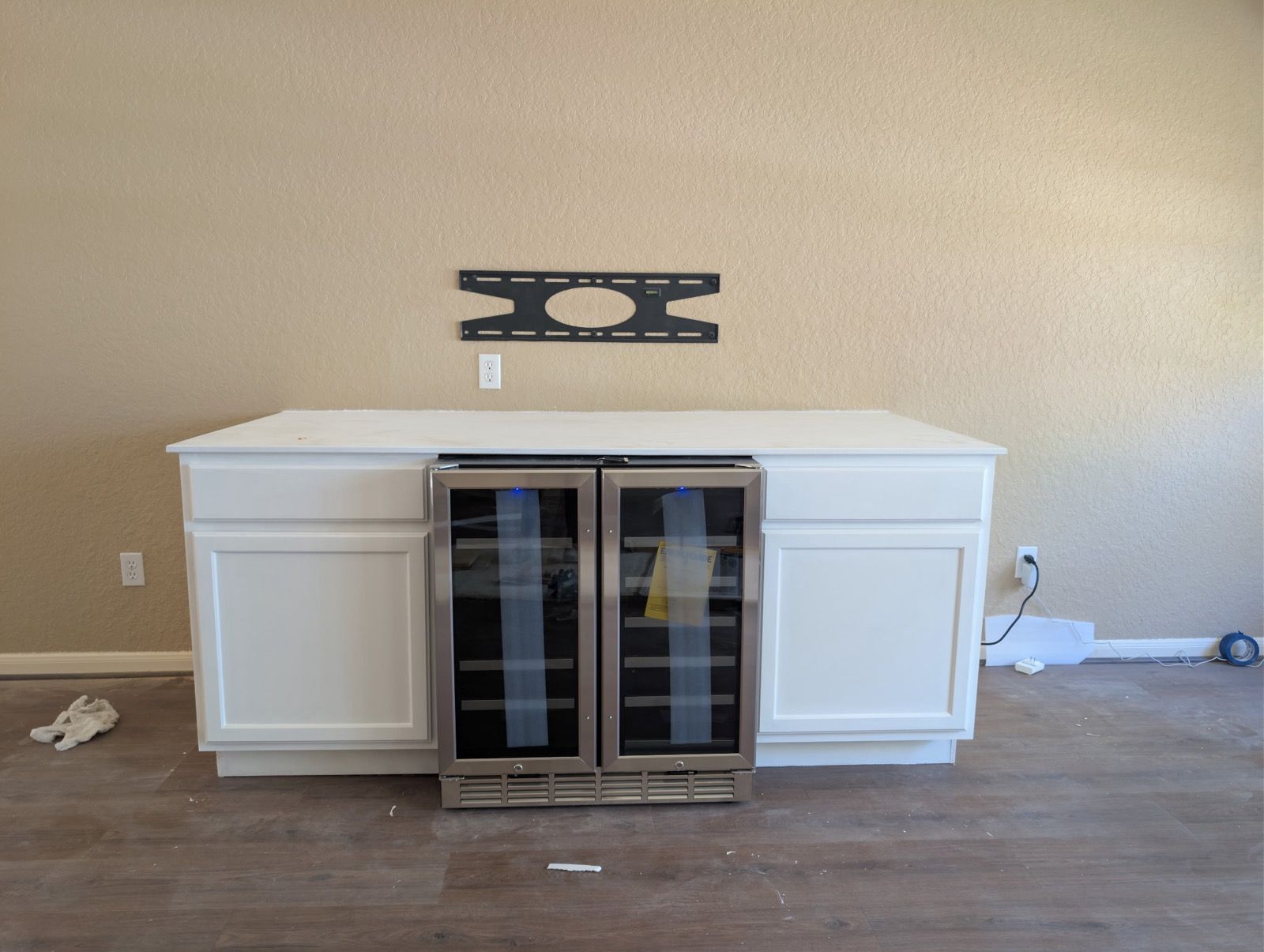 White cabinet with a built-in glass-front mini fridge in a mostly empty room against a beige wall.