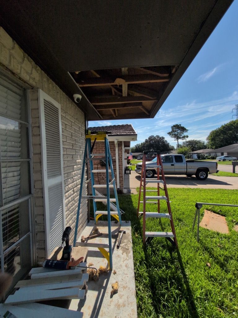 Ladders and tools beside a house under roof repair, with a pickup truck and yard in the background