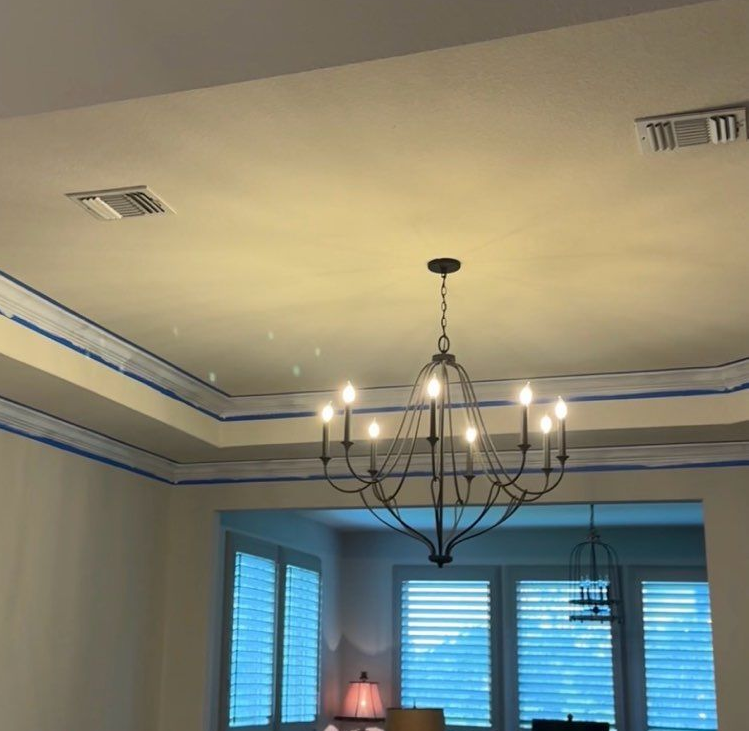 Living room ceiling with black chandelier and recessed vents above blue-trimmed windows