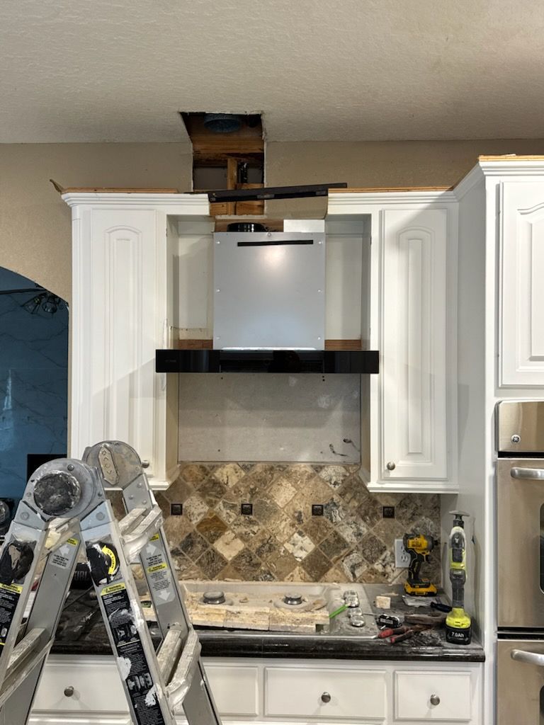 Kitchen with damaged ceiling above range hood, ladders in foreground, and unfinished backsplash area