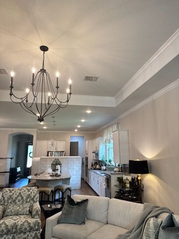 Bright open-concept living room with chandelier, white sofa, bar seating, and kitchen in the background.