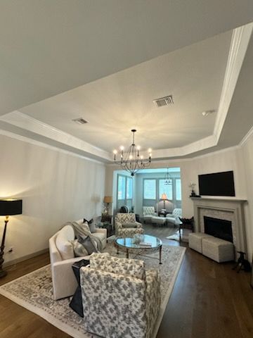 Elegant living room with gray sofas, patterned chairs, chandelier, fireplace, and large windows.