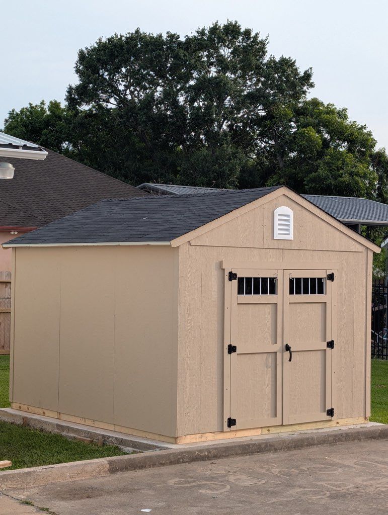 Beige outdoor storage shed with double doors and dark roof in a backyard.