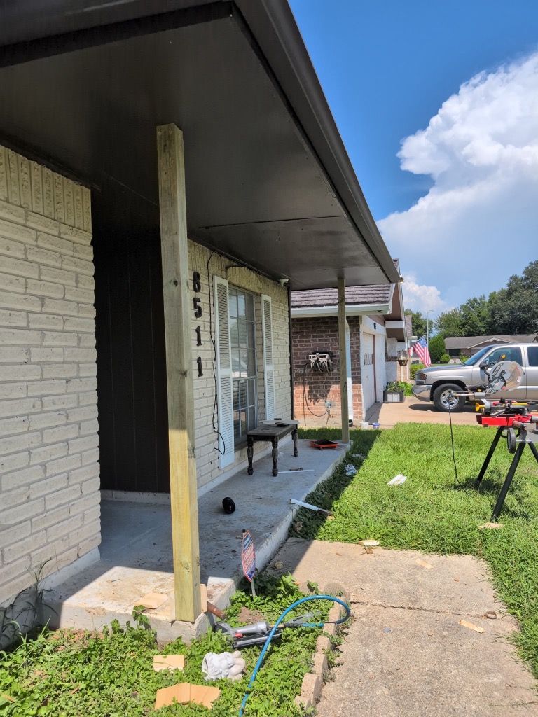 Covered porch of a house with a white brick wall, steps, and a walkway beside a grassy yard.