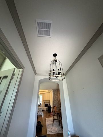 Narrow hallway with white walls, tray ceiling, pendant light, and arched doorway leading to a warm-lit room