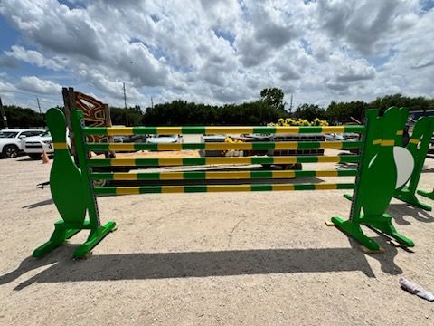Green-and-yellow horse jump obstacle on a paved outdoor lot under a cloudy sky