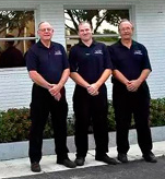 Three men are standing next to each other in front of a building.
