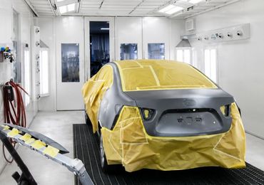 Car covered in yellow masking tape inside a white auto paint booth