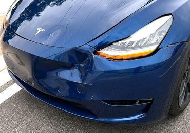 Damaged red car in an auto repair shop with hood open and front end exposed