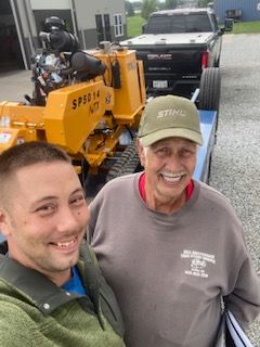 Two men are posing for a picture in front of a yellow tractor.