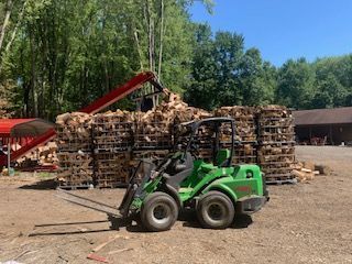 A green forklift is sitting in front of a pile of wood.
