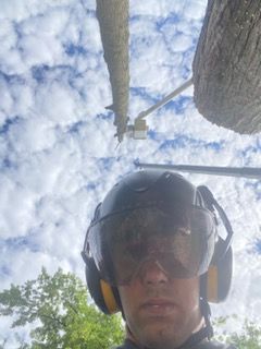 A man wearing a helmet and goggles is standing next to a tree.