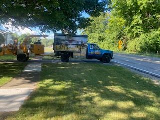 A blue truck is parked on the side of the road next to a tree stump grinder.