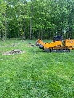 A yellow stump grinder is sitting in the middle of a lush green field.