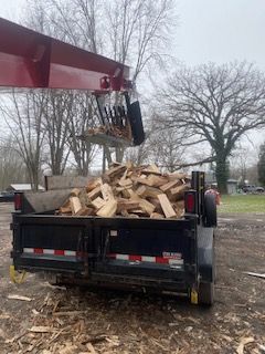 A crane is lifting a pile of wood from a trailer.