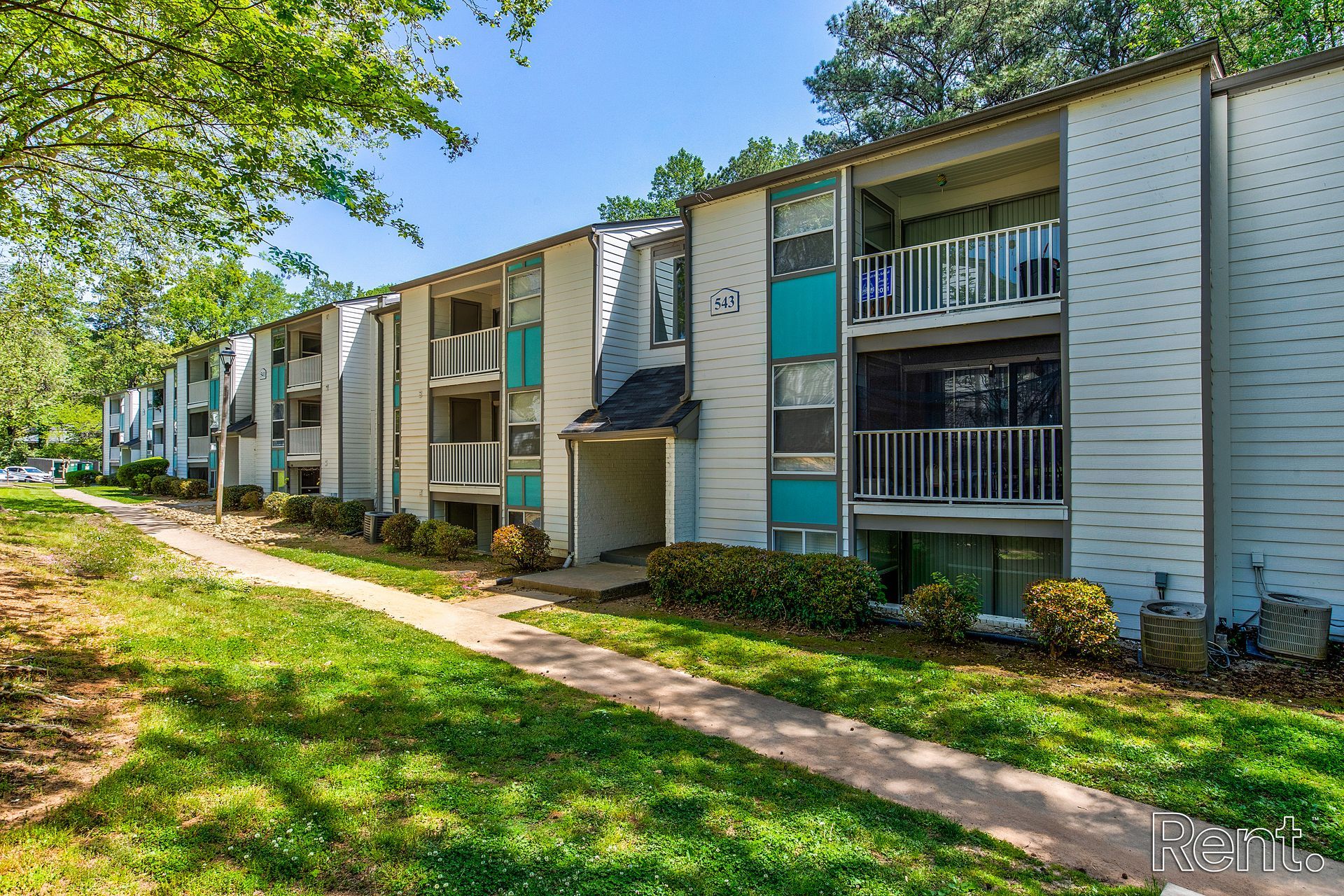 Apartment buildings beside a grassy walkway under trees on a sunny day