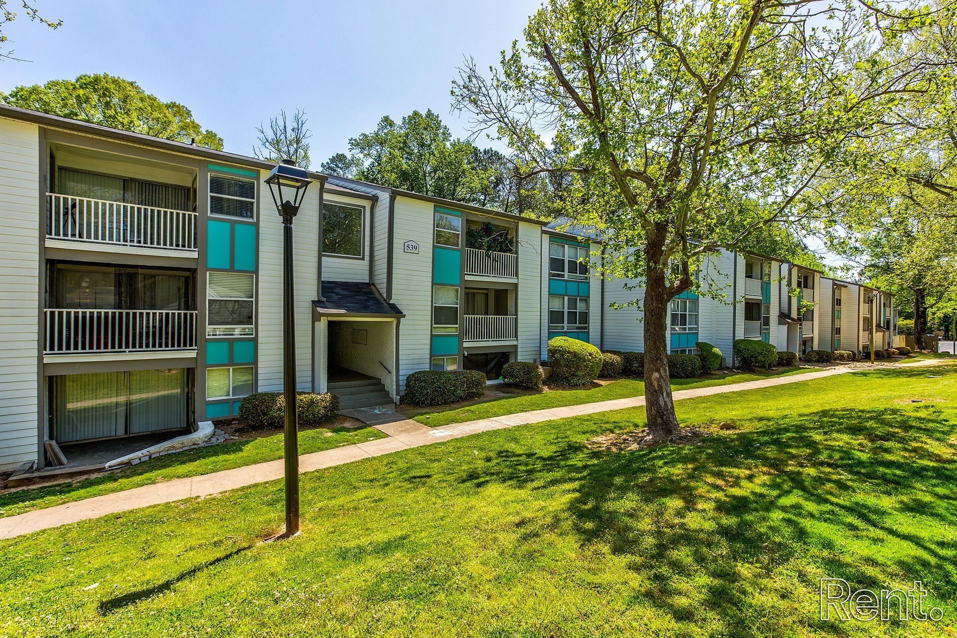 Apartment complex with teal balconies and a grassy courtyard lined with trees