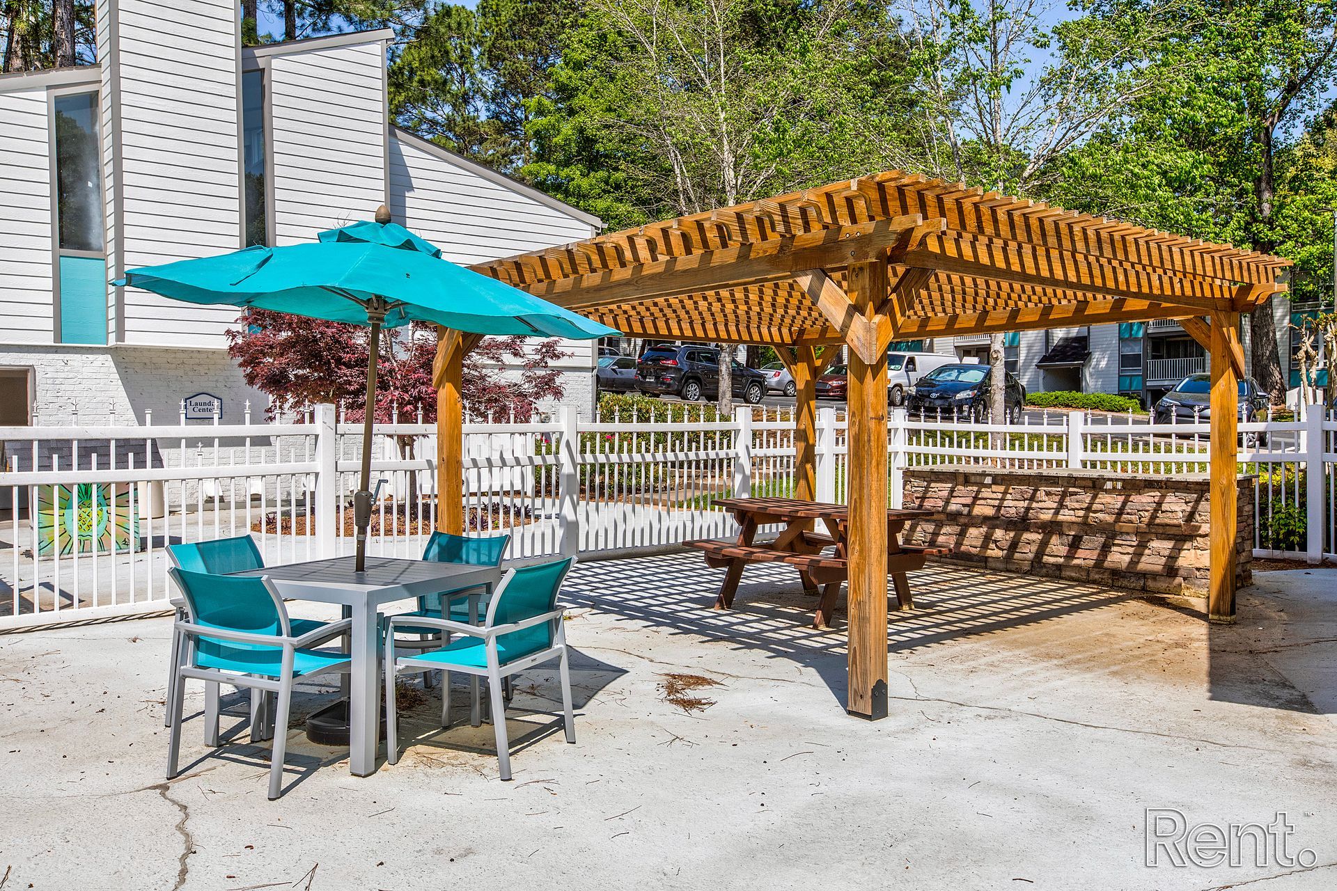 Patio with turquoise table and umbrella beside a wooden pergola and bench in a sunny courtyard