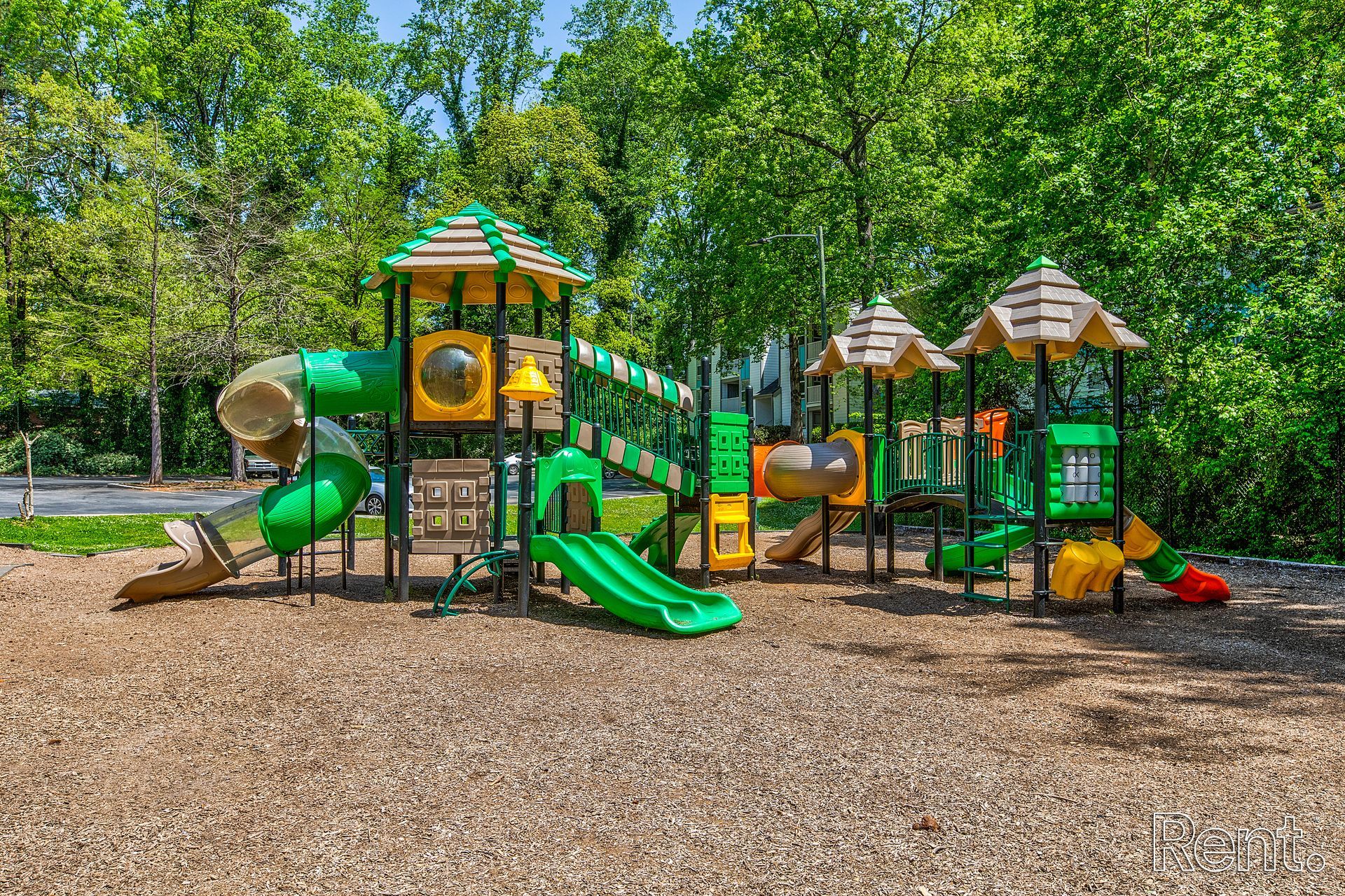 Colorful playground with slides and climbing structures on wood chips, surrounded by trees