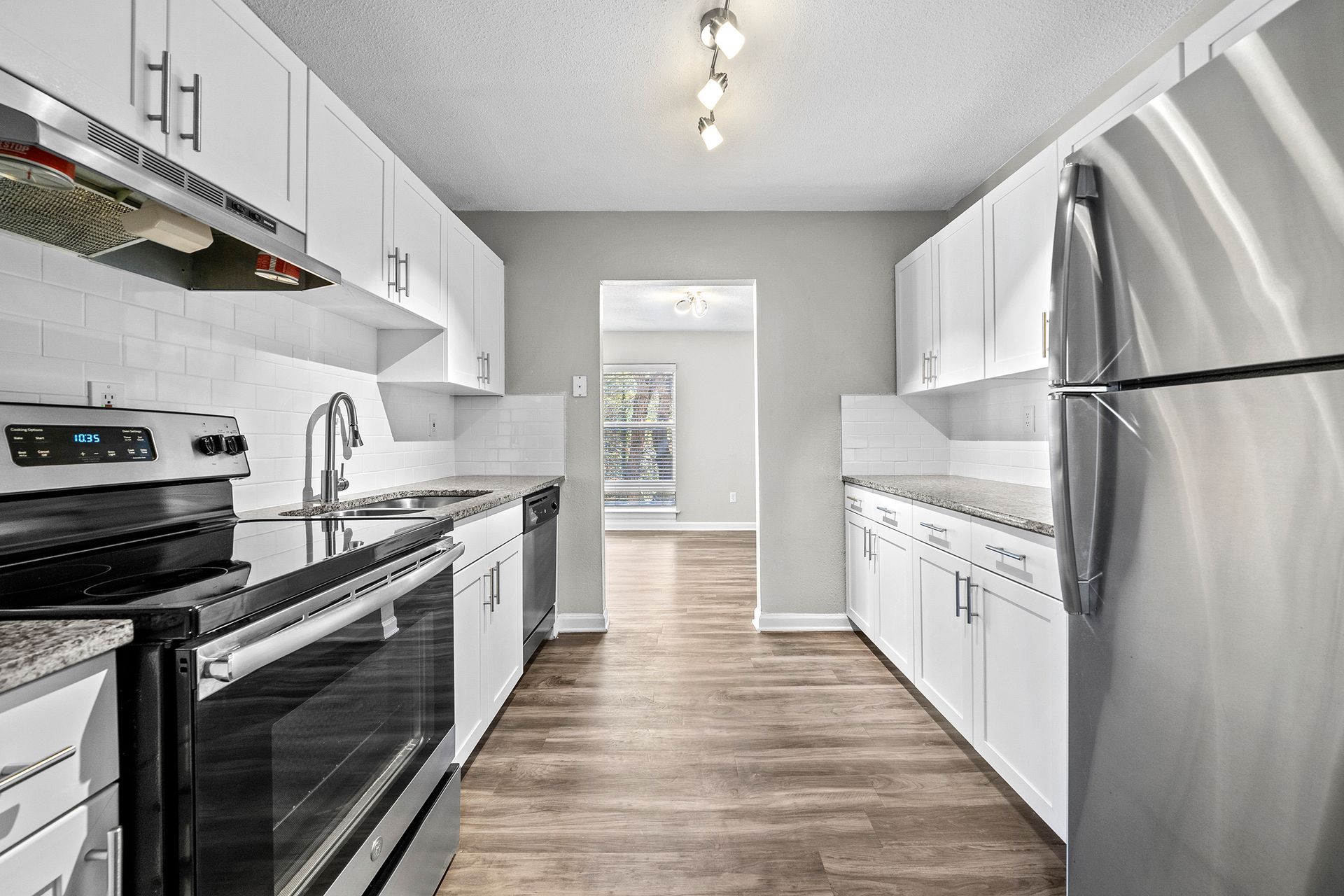 Modern white galley kitchen with stainless steel appliances and wood-look flooring