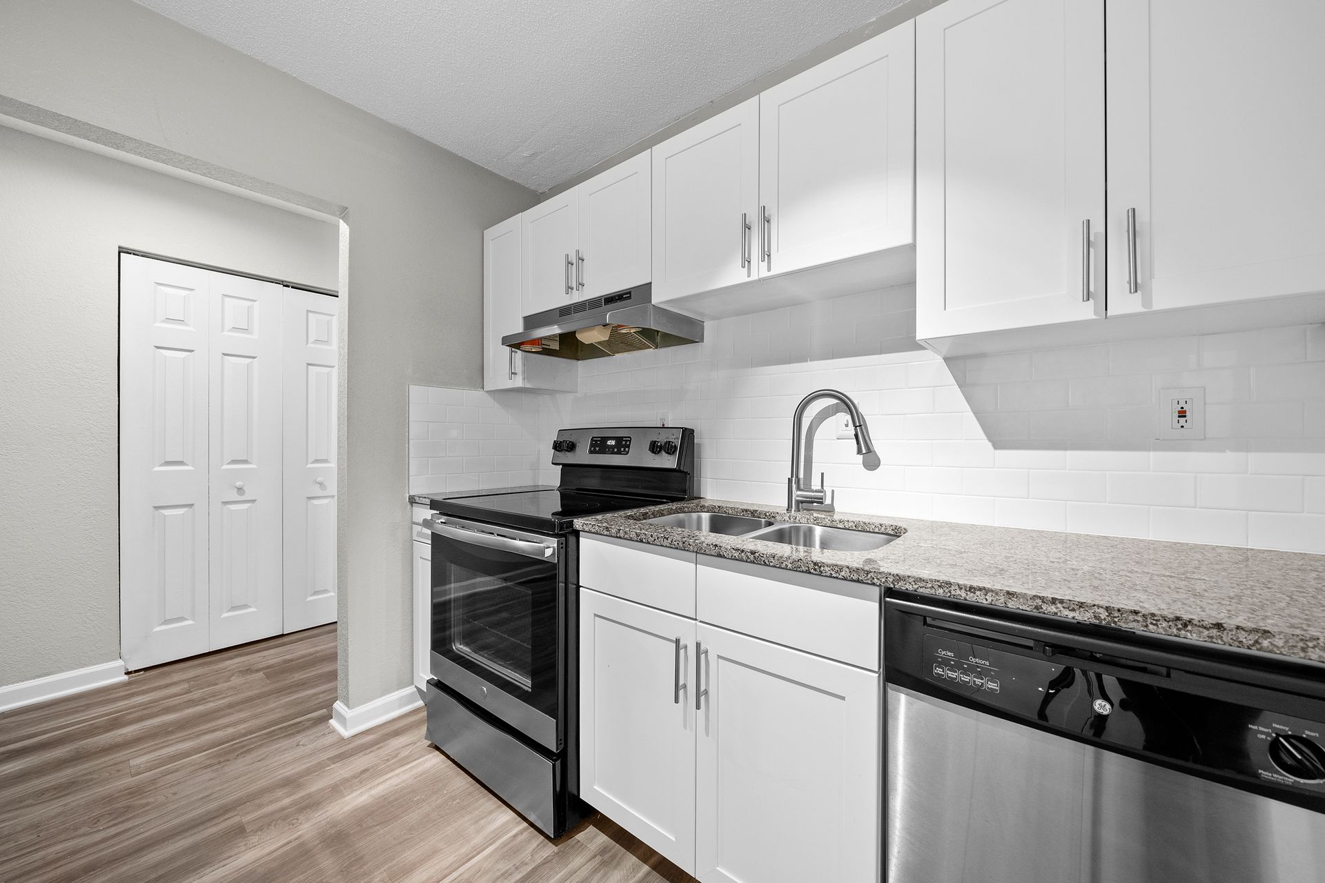 Modern white kitchen with stainless appliances, granite countertops, and light wood flooring