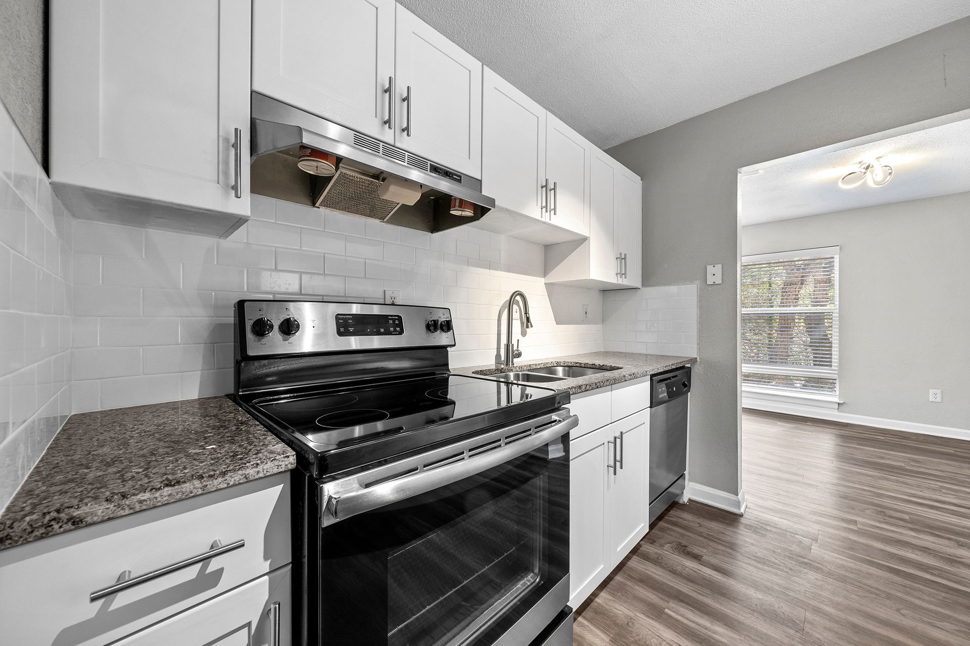 Modern white kitchen with granite countertops, stainless steel stove, and wood flooring
