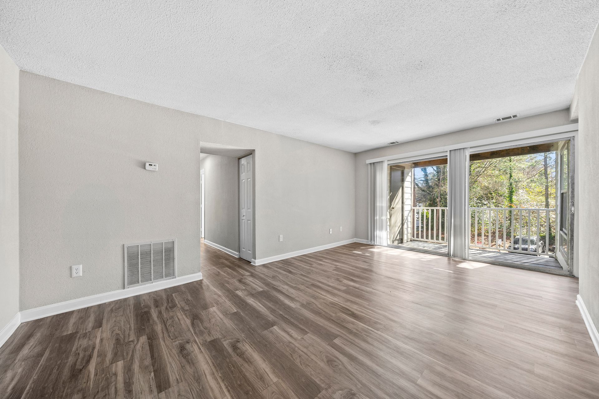 Empty modern living room with gray walls, wood floors, and sliding glass doors to a balcony.