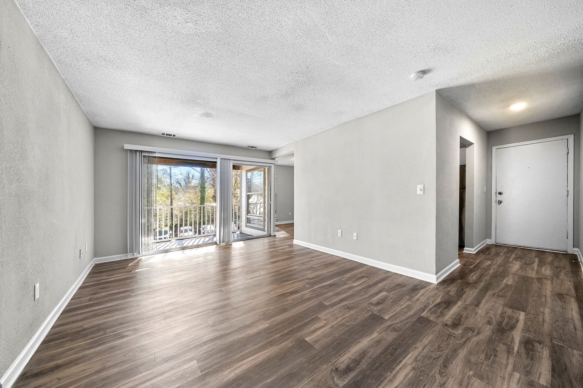 Empty modern living room with wood floors, light gray walls, and sliding glass doors to a balcony