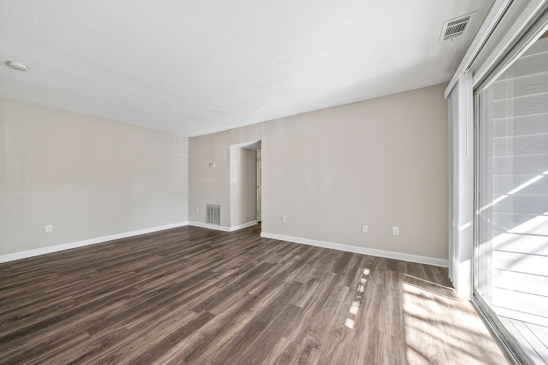 Empty living room with gray walls, wood-look flooring, and sliding glass doors letting in daylight