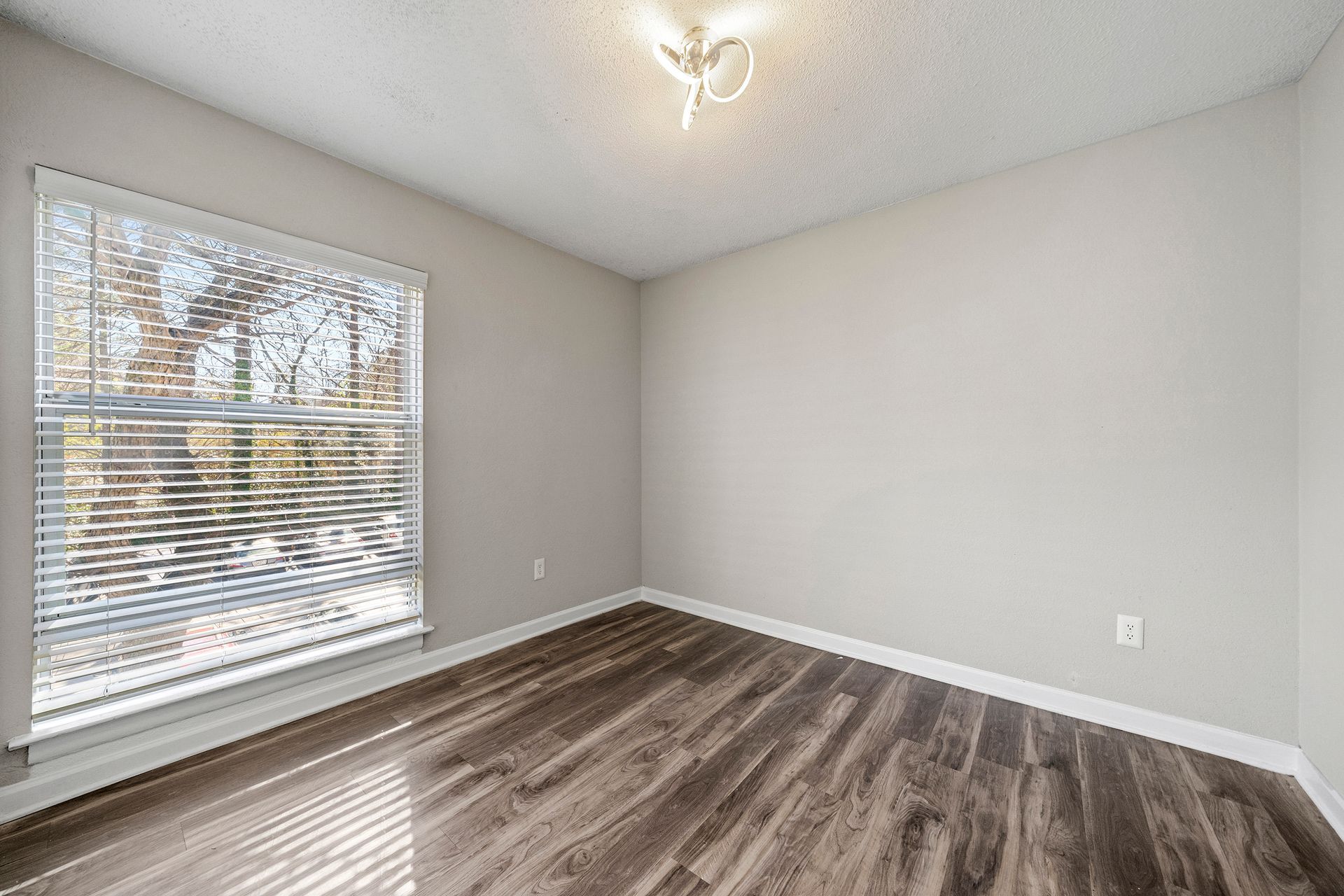 Empty room with gray walls, wood-look flooring, and a window with blinds letting in daylight.
