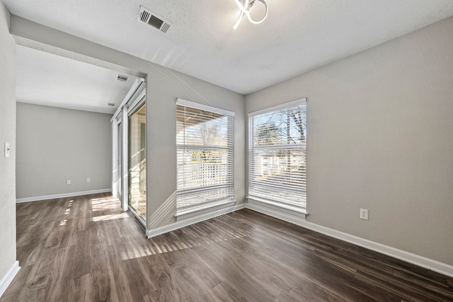 Bright empty room with dark wood floors, gray walls, and large windows letting in natural light