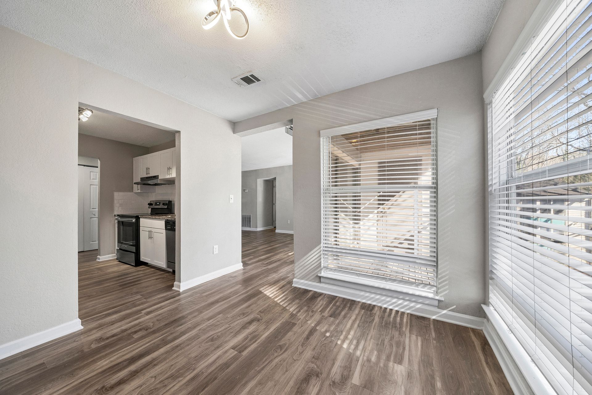 Empty modern room with gray walls, wood-look floors, and large windows with blinds.