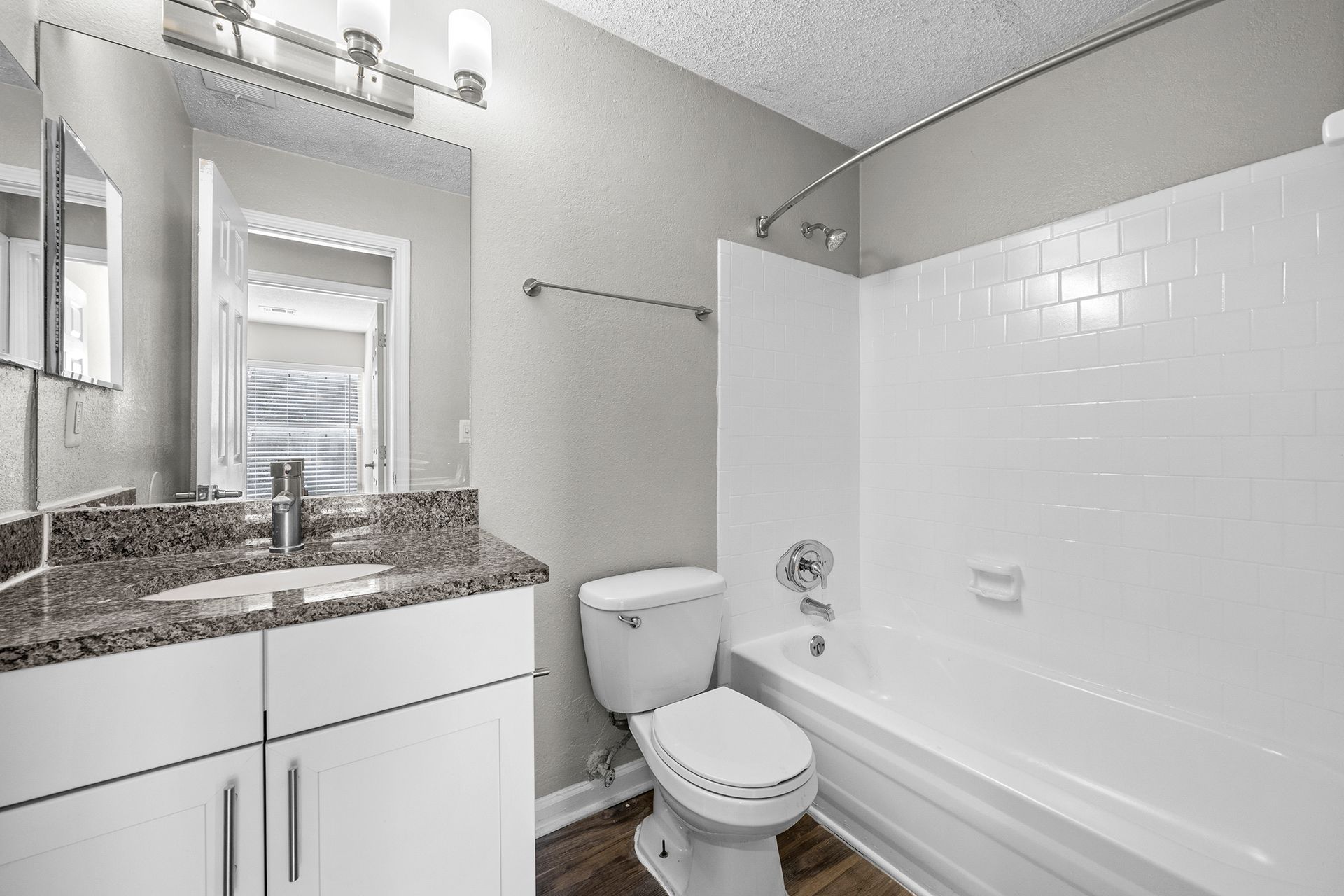 Bright bathroom with granite vanity, white tub, toilet, and window with blinds