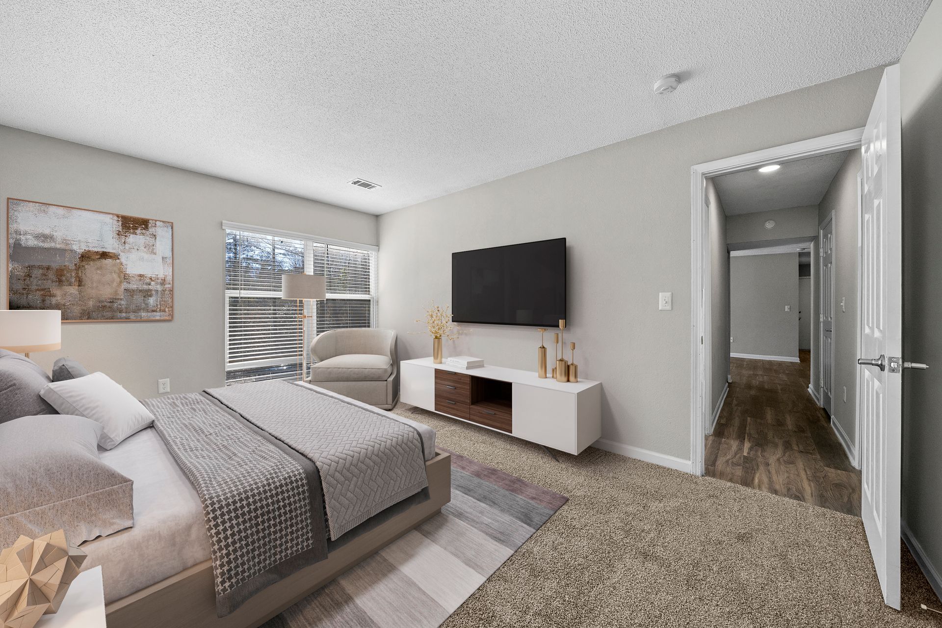 Bright bedroom with a bed, wall-mounted TV, and open doorway to a hallway.