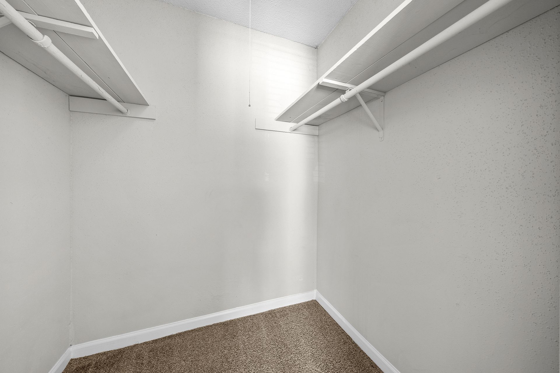 Empty white walk-in closet with wire shelves and beige carpet.
