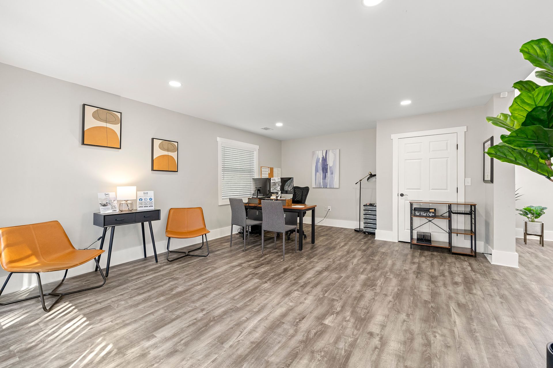 Bright modern waiting room with orange chairs, table, wood-look floor, and potted plant