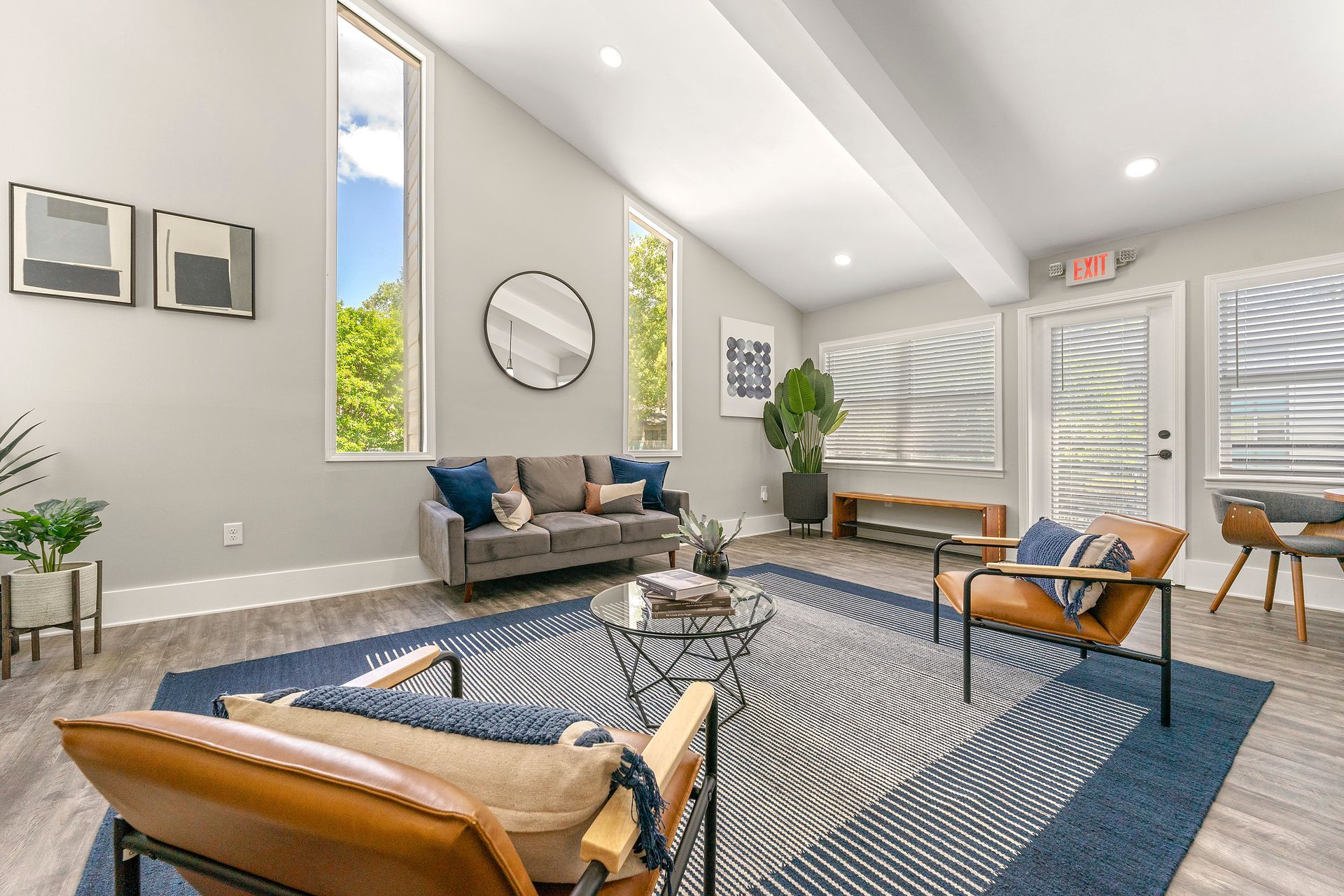 Bright modern living room with blue patterned rug, tan chairs, sofa, and large windows.