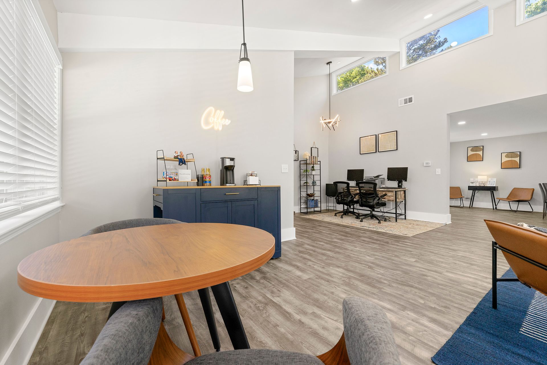 Bright open office lounge with round table, blue desk, workstations, and wood flooring