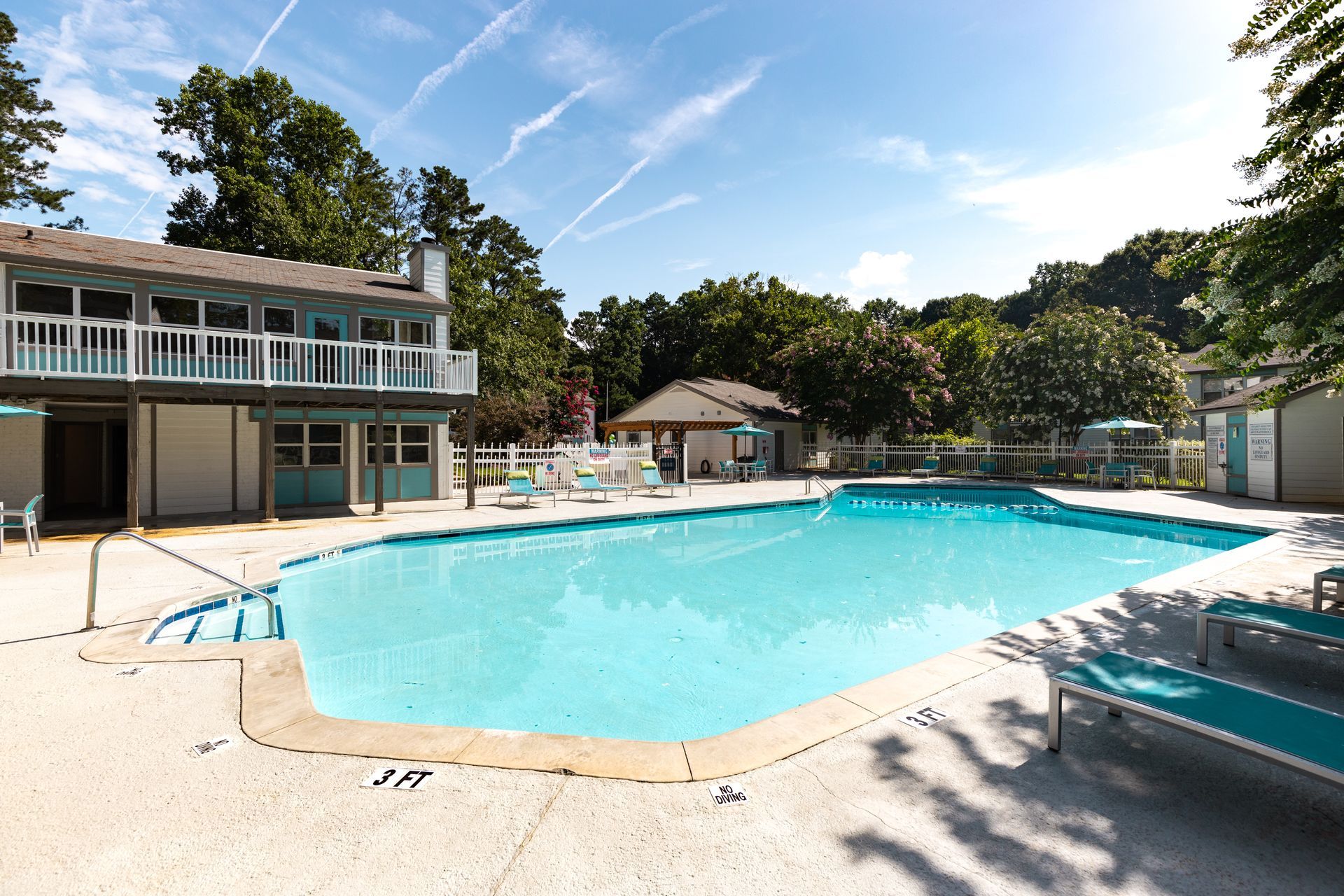 Outdoor swimming pool with turquoise water, lounge chairs, and a clubhouse under a clear blue sky