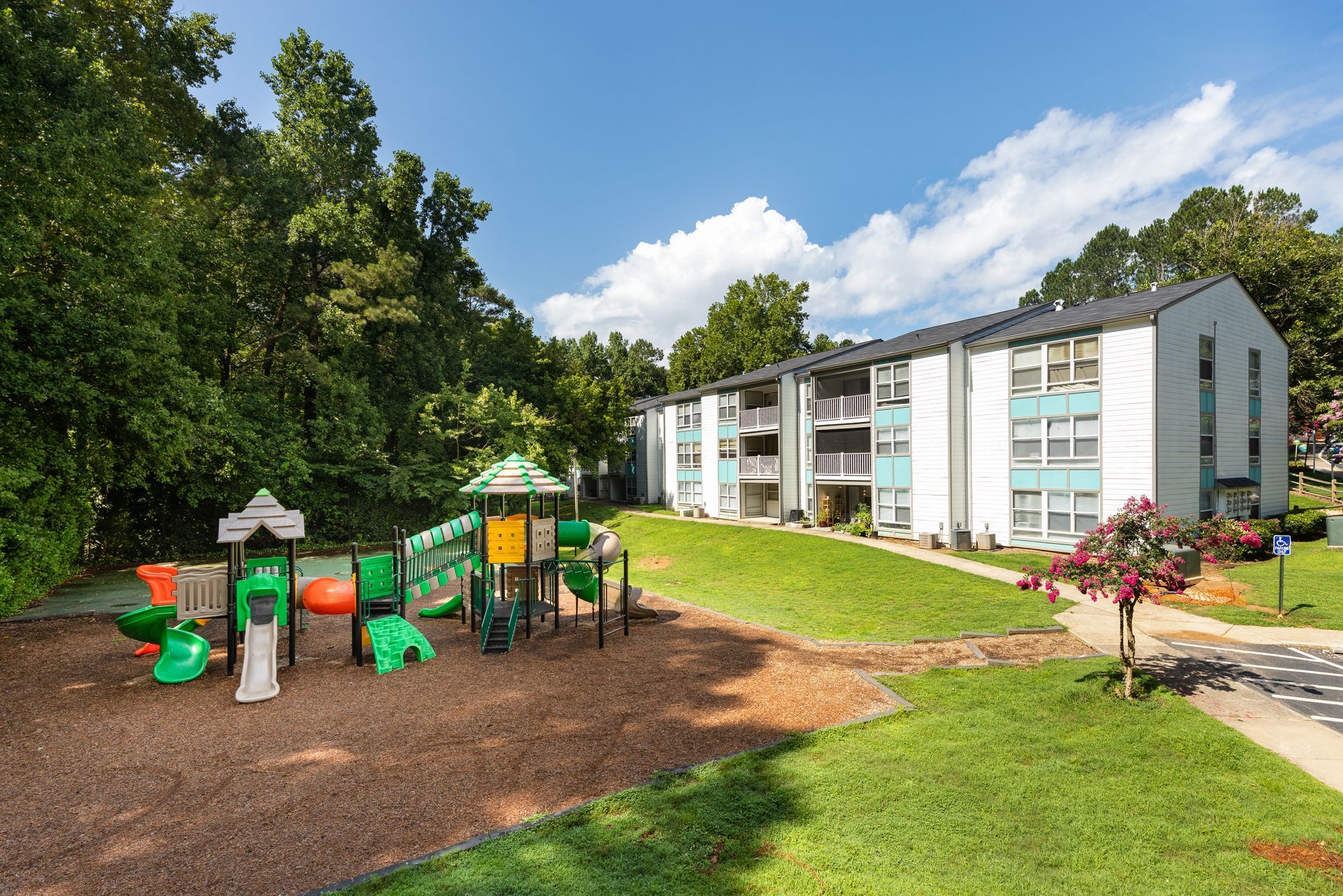 Apartment building beside a colorful playground and grassy courtyard on a sunny day