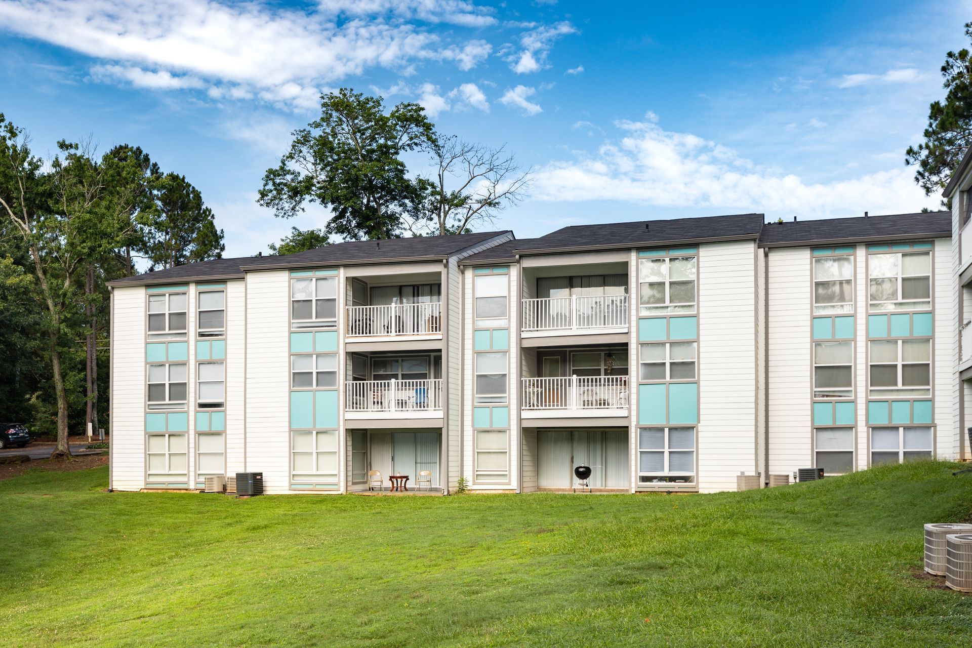 Apartment building with balconies and white siding beside a grassy lawn under a blue sky